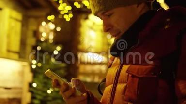 穿红色夹克的年轻人在晚上使用智能手机来<strong>抵御</strong>圣诞节的光照。 红色摄像机拍摄